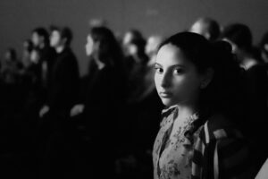 Fotoet viser en kvinde blandt mennesker. Siden handler om at være anderledes og fremmedgjort. Fotoet er taget af Justice Amoh.